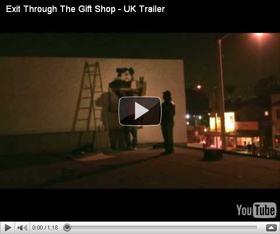 A dark urban rooftop scene shows a ladder leaning against a wall where a person is painting a black-and-white image. Another person stands nearby, observing. The environment is dimly lit by streetlights, with city buildings in the background. A YouTube video player interface is visible.